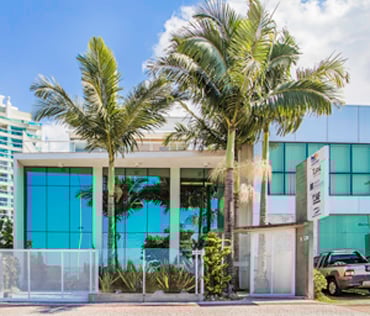 A vidraça do escritório reflete o jardim da fachada e o céu azul de Itajaí/SC.