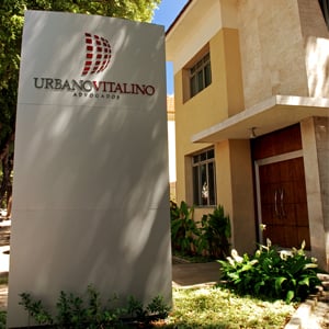 Em meio a árvores e plantas, uma placa na vertical indica o escritório da capital pernambucana, Recife.