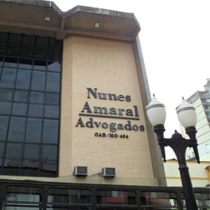 No centro do edifício em que se encontra o escritório de advocacia de Juiz de Fora/MG, a alta janela de vidro realça as paredes de tijolos à vista.