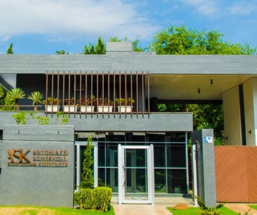 A entrada em tom cinza com detalhes marrons e o bem cuidado jardim ornamentam a fachada da banca em Lajeado/RS.