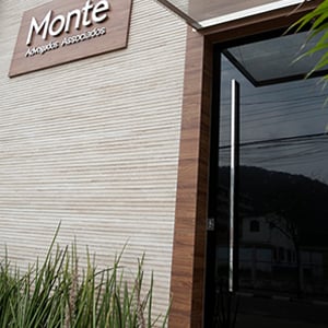 A placa de madeira com o nome do escritório do Guarujá/SP sobressai na parece texturizada. 