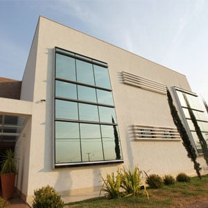 O bom tempo emoldura o cenário brasiliense. Na capital Federal, o escritório apresenta em sua estrutura grandes janelas espelhadas que refletem os pinheiros do verde jardim e elementos urbanos como os postes de luz.