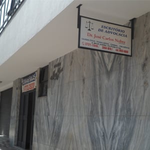 As letras em azul e vermelho da placa do escritório de Poços de Caldas/MG se destacam ao lado da parde de mámore acinzentado. 