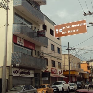 Na sacada revestida de pastilhas, a placa da banca de São Roque/SP alinha-se à placa que informa a direção das igrejas da cidade. 