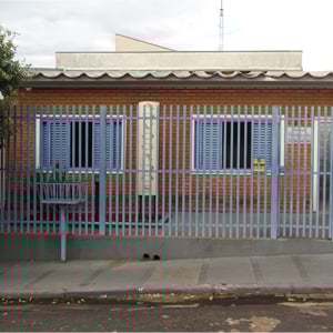 Por entre as grades cinza, a placa mostra que a casa de tijolos à vista em Cassilândia/MS é um escritório de advocacia. 