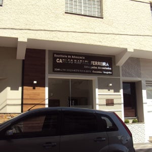 No painel de madeira, a letras prateadas que formam o nome do escritório de Caxambu/MG são realçadas pela luz do sol. 